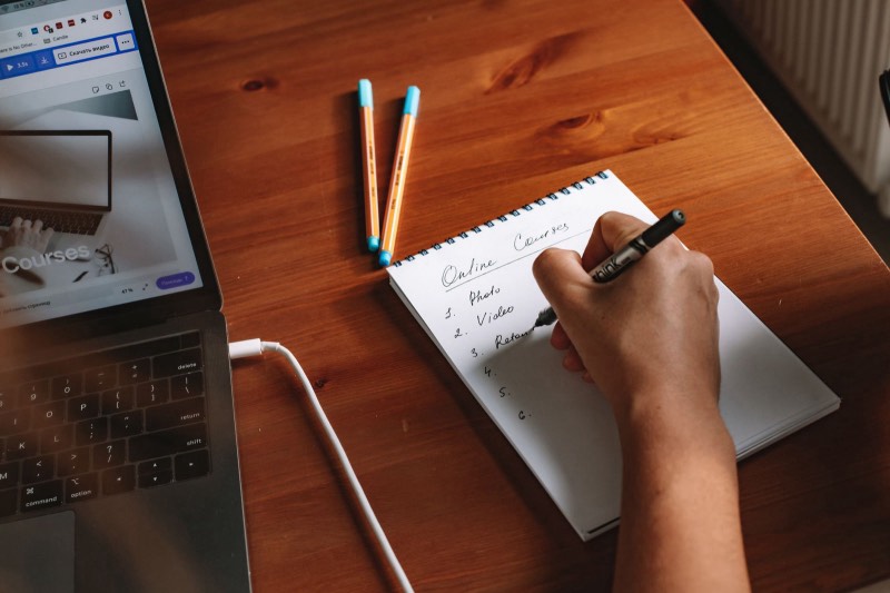 Main écrivant une liste de cours en ligne près d'un ordinateur portable